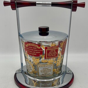 May include: Vintage cocktail ice bucket with a chrome and red base, handle, and lid. The glass bucket features gold and red text with cocktail recipes for Old Fashioned, Bacardi, and Manhattan drinks.
