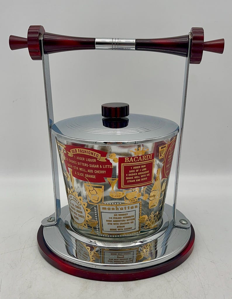May include: Vintage cocktail ice bucket with a chrome and red base, handle, and lid. The glass bucket features gold and red text with cocktail recipes for Old Fashioned, Bacardi, and Manhattan drinks.