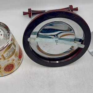 May include: An assortment of barware items, including a glass tumbler with gold and red accents, a chrome ice bucket with a dark wood rim, and a chrome lid with a red knob. The ice bucket has a chrome interior and a dark wood handle.
