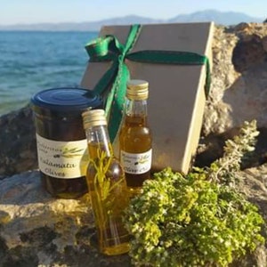 K&ouml;nnte beinhalten: Eine Geschenkbox mit gr&uuml;nem Band und Schleife, die ein Glas Kalamata-Oliven und zwei Flaschen Oliven&ouml;l enth&auml;lt. Die Flaschen sind mit "Trimino" und "Oliven&ouml;l" beschriftet.