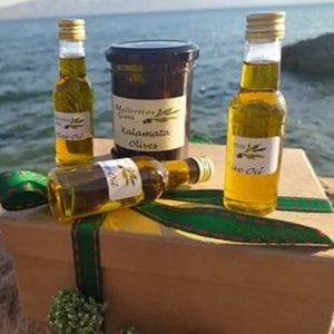 K&ouml;nnte beinhalten: Eine Geschenkbox gef&uuml;llt mit Oliven&ouml;l und Kalamata-Oliven. Die Box ist mit einem gr&uuml;n-roten Band verziert. Die Oliven&ouml;lflaschen sind aus klarem Glas mit einem gr&uuml;nen Etikett. Die Oliven befinden sich in einem Glasgef&auml;&szlig; mit einem schwarzen Etikett, auf dem "Kalamata Olives" steht.