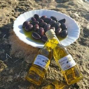 K&ouml;nnte beinhalten: Zwei durchsichtige Glasflaschen Oliven&ouml;l mit Etiketten, auf denen "Mediterranean Extra Virgin Olive Oil" steht. Die Flaschen stehen auf einem wei&szlig;en Teller mit einem Haufen schwarzer Oliven.