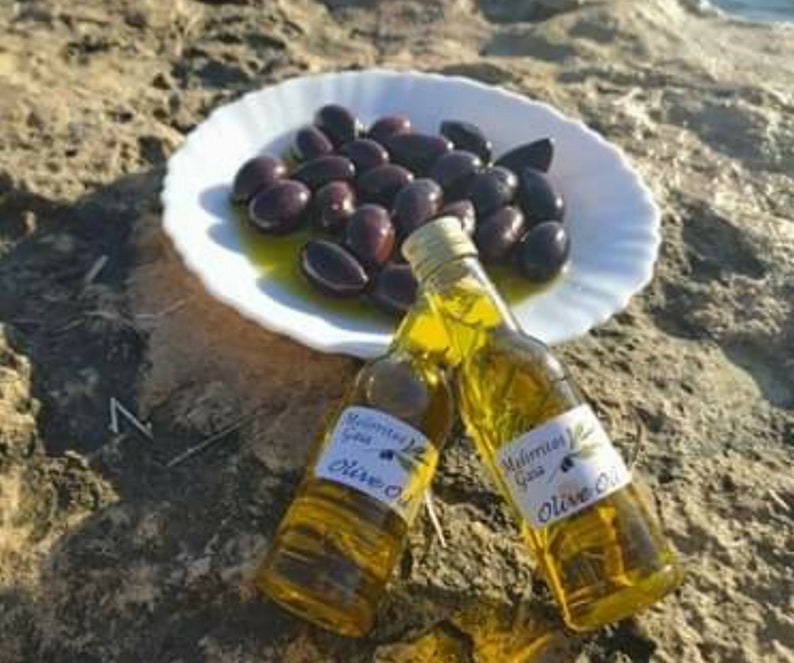 K&ouml;nnte beinhalten: Zwei durchsichtige Glasflaschen Oliven&ouml;l mit Etiketten, auf denen "Mediterranean Extra Virgin Olive Oil" steht. Die Flaschen stehen auf einem wei&szlig;en Teller mit einem Haufen schwarzer Oliven.