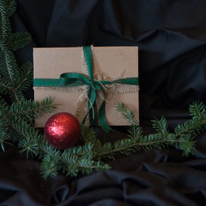 May include: A brown gift box with a green and red ribbon and a red ornament on a black background.