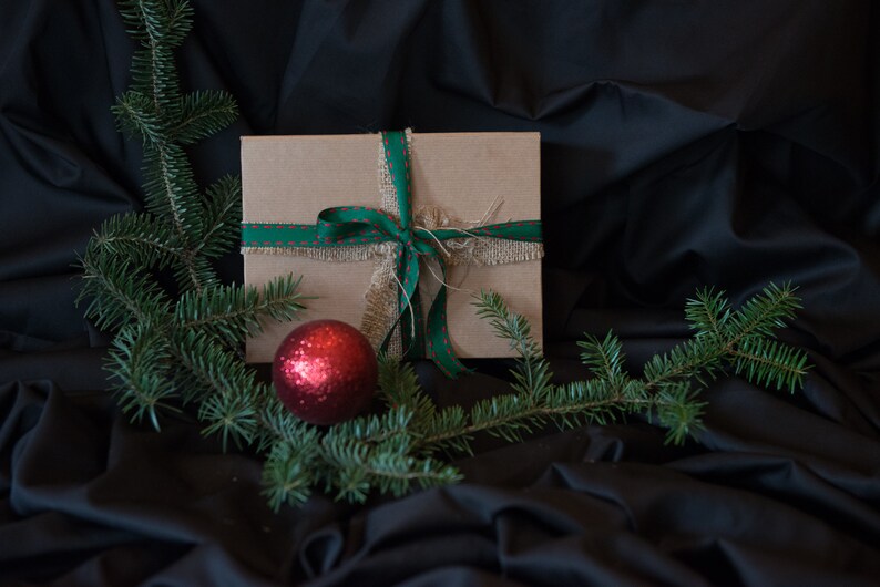 May include: A brown gift box with a green and red ribbon and a red ornament on a black background.