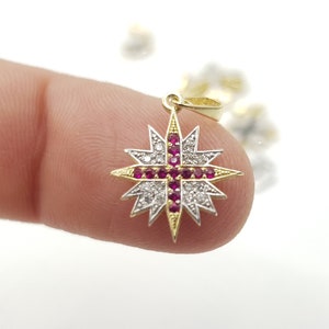 Puede incluir: Un colgante de oro con un diseño de estrella. La estrella está engastada con pequeñas piedras transparentes y una cruz roja en el centro.