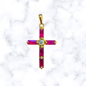 May include: A gold cross pendant with a clear diamond in the center and red ruby stones around the edges.