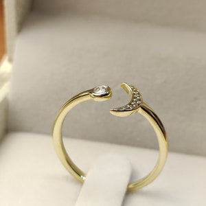 Op de afbeelding: Een gouden ring met een halve maan ontwerp bezet met kleine diamanten. De ring is aan één kant open en heeft aan de andere kant een enkele diamant.