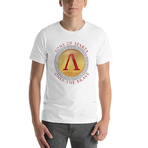 Op de afbeelding: Wit T-shirt met een rode en gouden Spartanen schild afbeelding. Het schild heeft een rode letter 'A' erin. De tekst 'Sons of Sparta' en 'Only the Brave' omringt het schild.