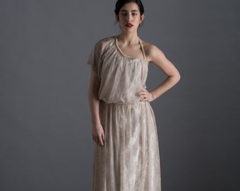 May include: A woman wearing a white lace dress with a one-shoulder neckline and a pearl embellishment. The dress has a flowing skirt and is cinched at the waist.