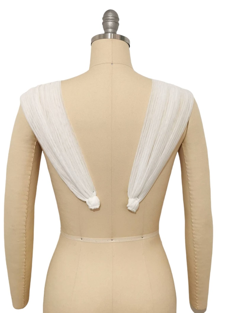 May include: White sheer fabric draped over a dress form, creating a V-shaped neckline and flowing sleeves.