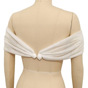 May include: White off-the-shoulder bridal shawl made of sheer fabric with a knotted detail at the back.