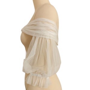 May include: White off-the-shoulder tulle bridal bolero with puffed sleeves and a ruffled trim.