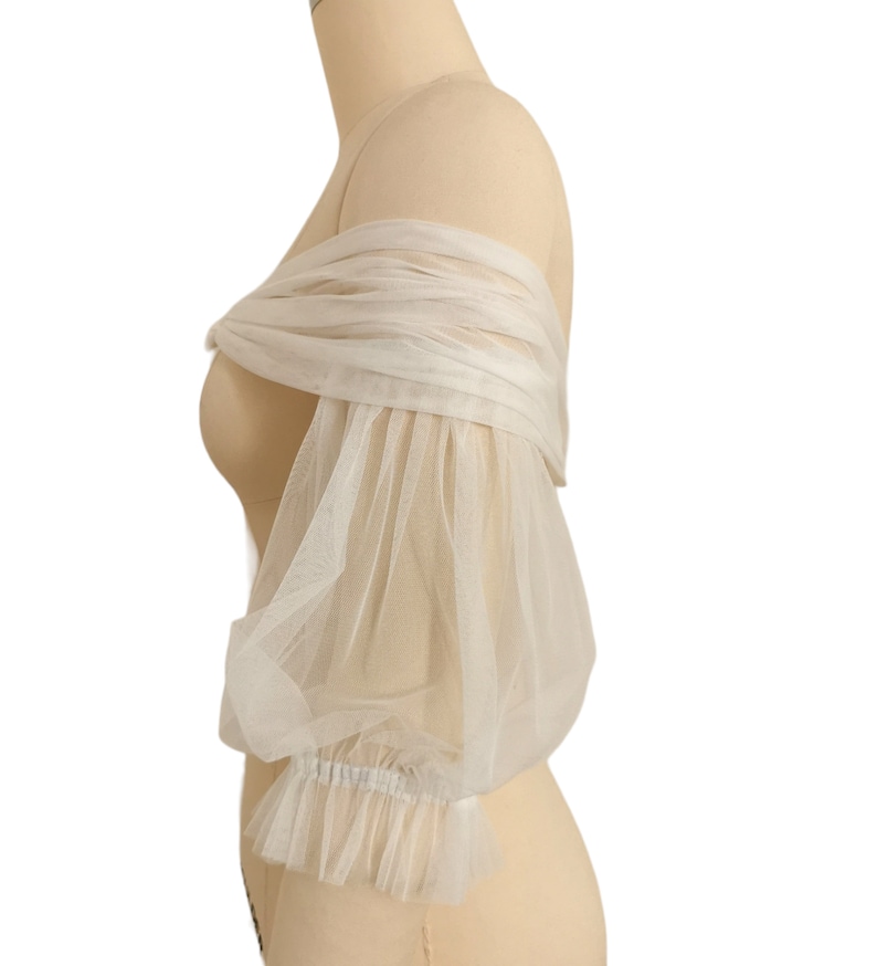 May include: White off-the-shoulder tulle bridal bolero with puffed sleeves and a ruffled trim.
