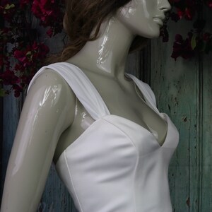 May include: A white sleeveless dress featuring a sweetheart neckline and wide shoulder straps. The bodice is constructed with vertical seams that provide structure, and the fabric has a smooth, matte finish. The dress is displayed on a mannequin.