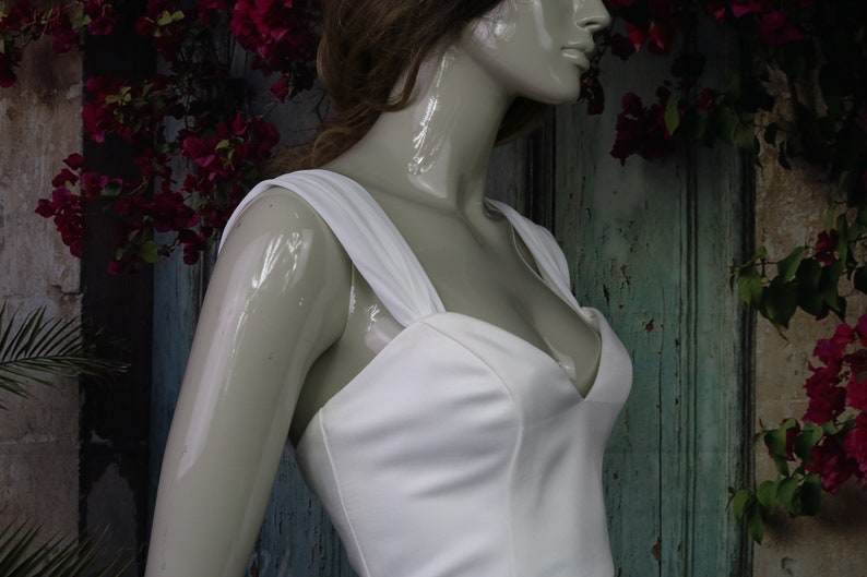 May include: A white sleeveless dress featuring a sweetheart neckline and wide shoulder straps. The bodice is constructed with vertical seams that provide structure, and the fabric has a smooth, matte finish. The dress is displayed on a mannequin.