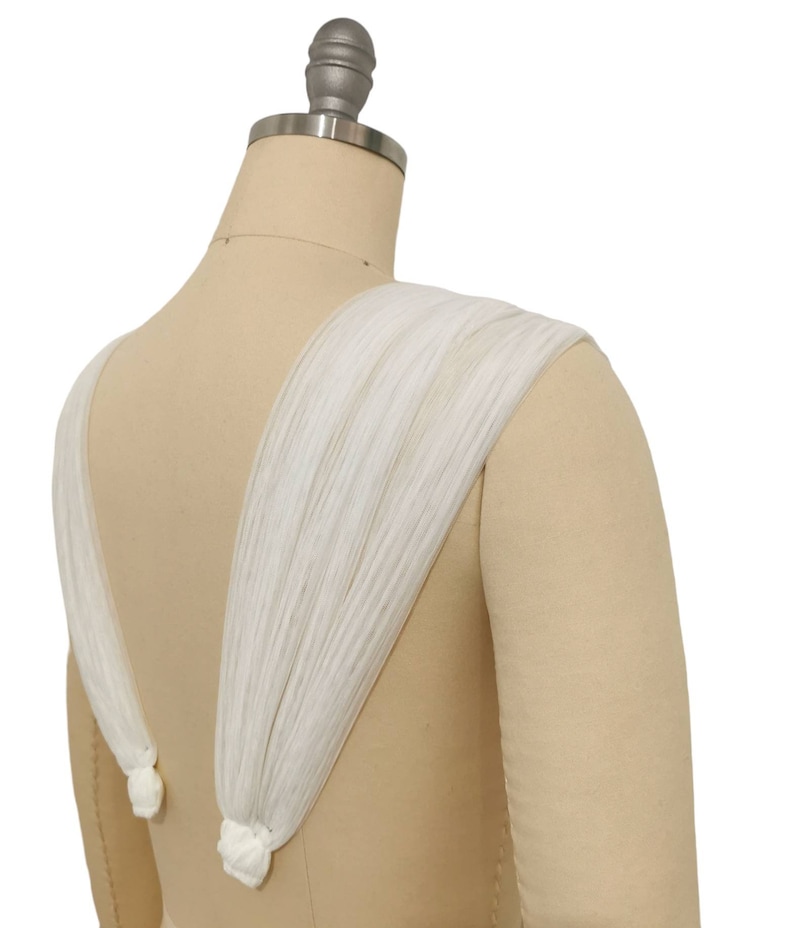 May include: White fabric straps with a gathered detail at the back of a dress form.