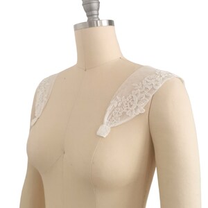 Puede incluir: Tirantes de hombro de encaje blanco con bordado floral. Las tiras son de tela transparente y tienen un aspecto delicado y femenino.