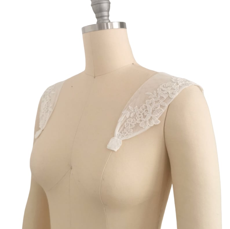Puede incluir: Tirantes de hombro de encaje blanco con bordado floral. Las tiras son de tela transparente y tienen un aspecto delicado y femenino.