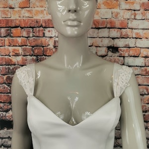 May include: White strapless wedding dress bodice with a sweetheart neckline and lace straps. The bodice is made of a smooth, satin-like fabric.