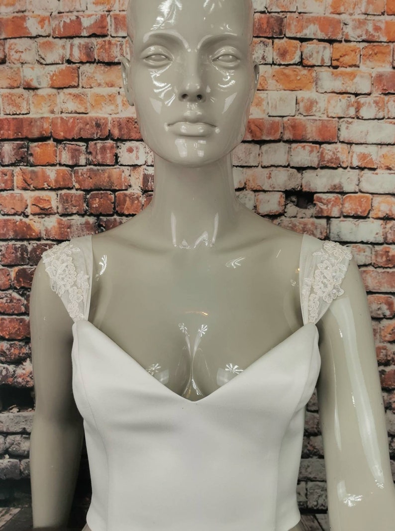 May include: White strapless wedding dress bodice with a sweetheart neckline and lace straps. The bodice is made of a smooth, satin-like fabric.