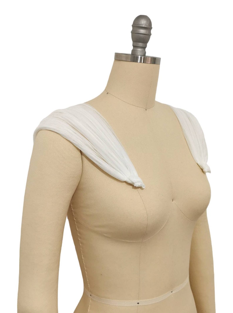 May include: White tulle shoulder straps for a wedding dress or other formal attire. The straps are gathered and tied at the shoulders.