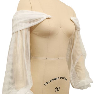Puede incluir: Mangas blancas transparentes de hombros descubiertos con un detalle fruncido en la parte superior e inferior. Las mangas est&aacute;n hechas de una tela ligera y tienen un aspecto delicado y fluido. "COLLAPSIBLE SHOULDER 10" est&aacute; escrito en el maniqu&iacute;.