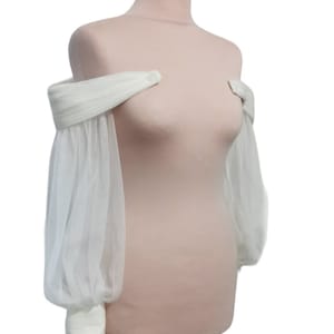 Puede incluir: Un bolero de novia blanco de tul sin hombros con mangas largas y abullonadas.
