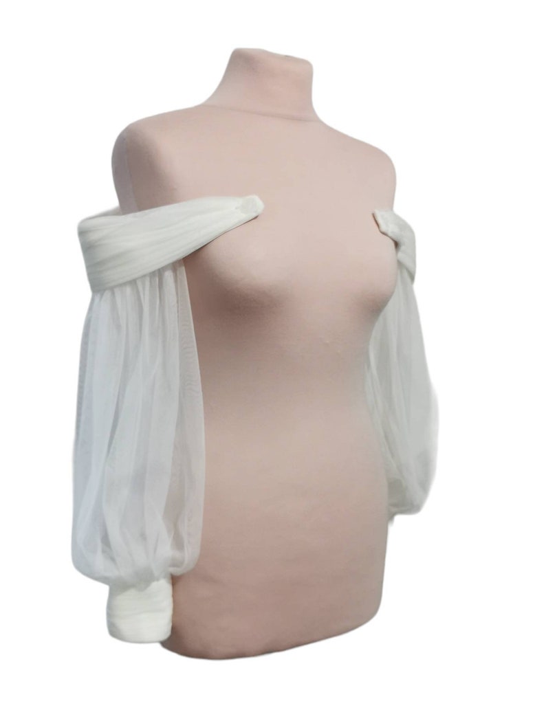 Puede incluir: Un bolero de novia blanco de tul sin hombros con mangas largas y abullonadas.