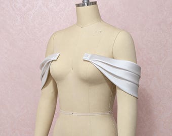 May include: A pair of white satin off-the-shoulder sleeves featuring a pleated design and small white buttons at the top edge. The sleeves are displayed on a beige mannequin torso, showing the fabric draped around the upper arms.