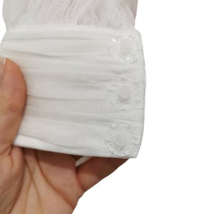 Puede incluir: Tela de tul blanca con tres botones de pl&aacute;stico transparente. La tela est&aacute; fruncida en la parte superior y los botones est&aacute;n espaciados uniformemente a lo largo del borde inferior.