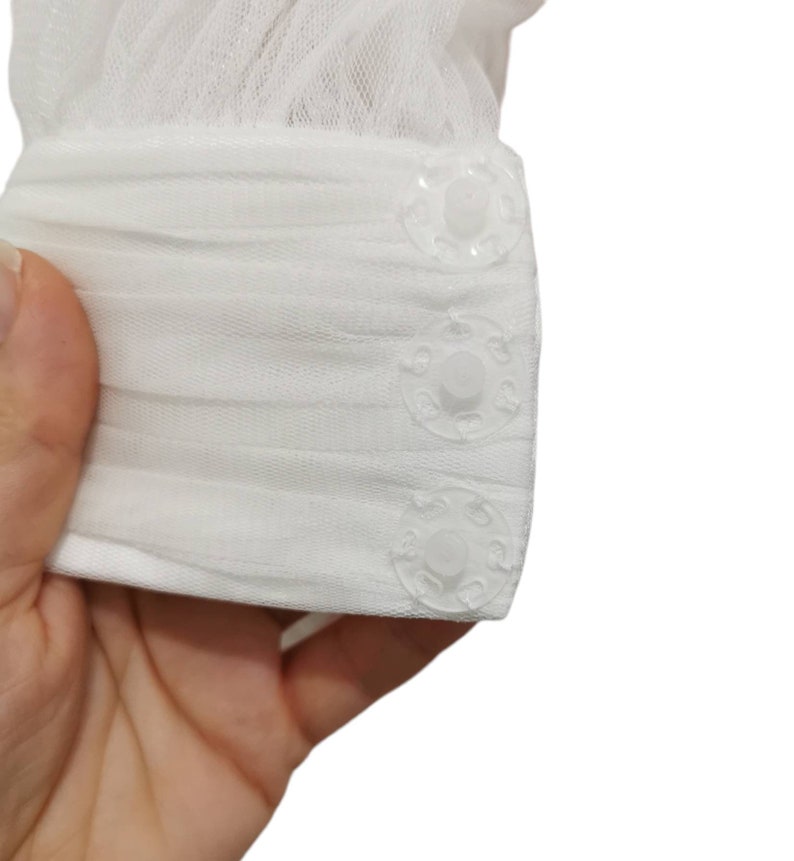 Puede incluir: Tela de tul blanca con tres botones de pl&aacute;stico transparente. La tela est&aacute; fruncida en la parte superior y los botones est&aacute;n espaciados uniformemente a lo largo del borde inferior.