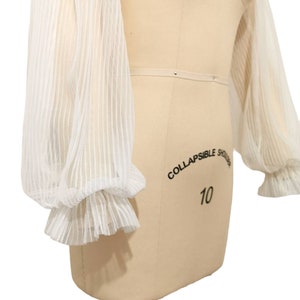 Puede incluir: Blusa blanca transparente con mangas largas abullonadas y ribete de volantes. Las mangas est&aacute;n hechas de una tela delicada y ligera, perfecta para superponer.