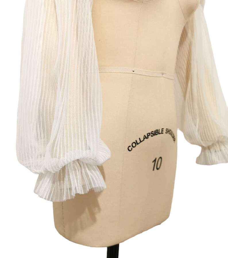 Puede incluir: Blusa blanca transparente con mangas largas abullonadas y ribete de volantes. Las mangas est&aacute;n hechas de una tela delicada y ligera, perfecta para superponer.