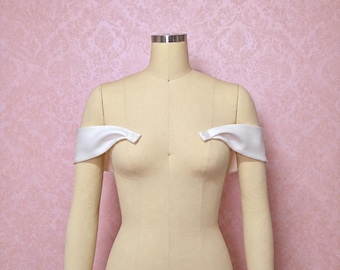 May include: A pair of white satin off-the-shoulder sleeves displayed on a beige dress form. The sleeves feature a smooth, lustrous finish and are positioned to drape across the upper arms, creating a clean, structured look for formal attire.