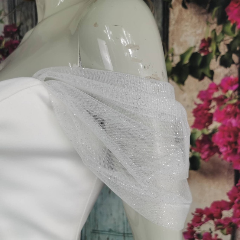 May include: White off-the-shoulder dress with a sheer, sparkly tulle overlay on the shoulders.