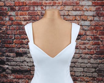 May include: A solid white sleeveless dress featuring a deep V-neckline and wide shoulder straps. The garment is displayed on a mannequin, showcasing a clean, smooth fabric texture and a fitted bodice design that extends downward.