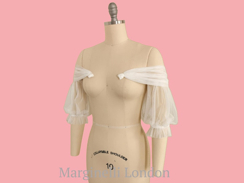 May include: White off-the-shoulder sheer fabric sleeves with ruched detailing and a gathered elastic band at the top. The sleeves are on a dress form with the text "Collapsible Shoulder" and "Margareti London" on the base.