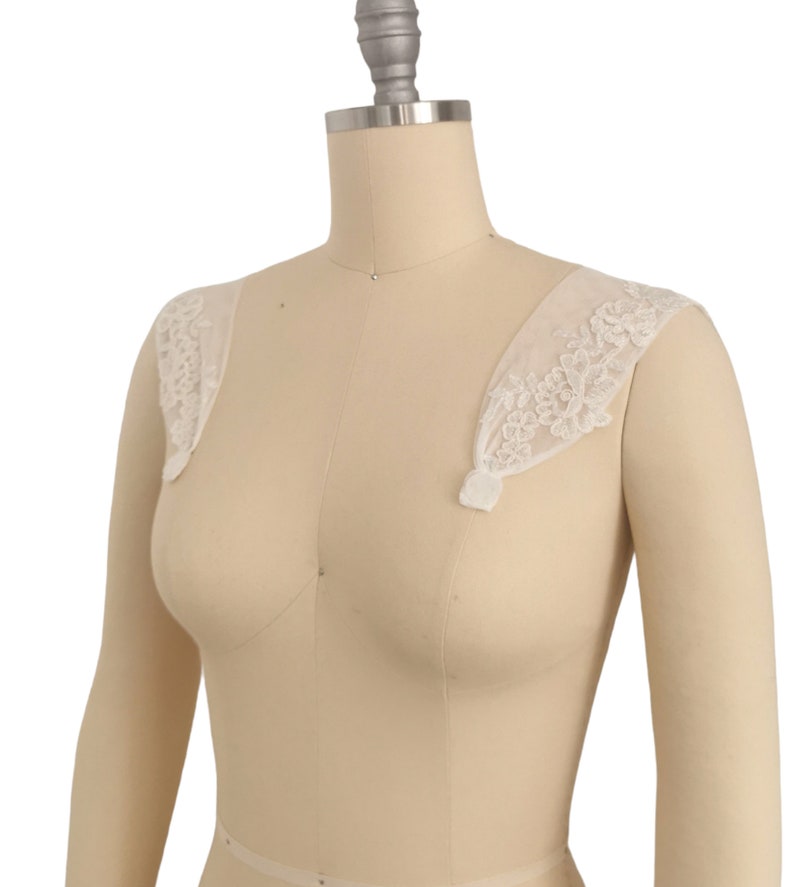 Puede incluir: Tirantes de hombro de encaje blanco con un delicado patr&oacute;n floral. Las tiras son de tela transparente y est&aacute;n dise&ntilde;adas para usarse sobre un vestido o una blusa.