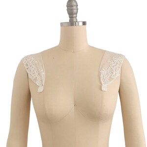 Puede incluir: Un par de tirantes de hombro de encaje blanco para un vestido de novia u otra vestimenta formal.