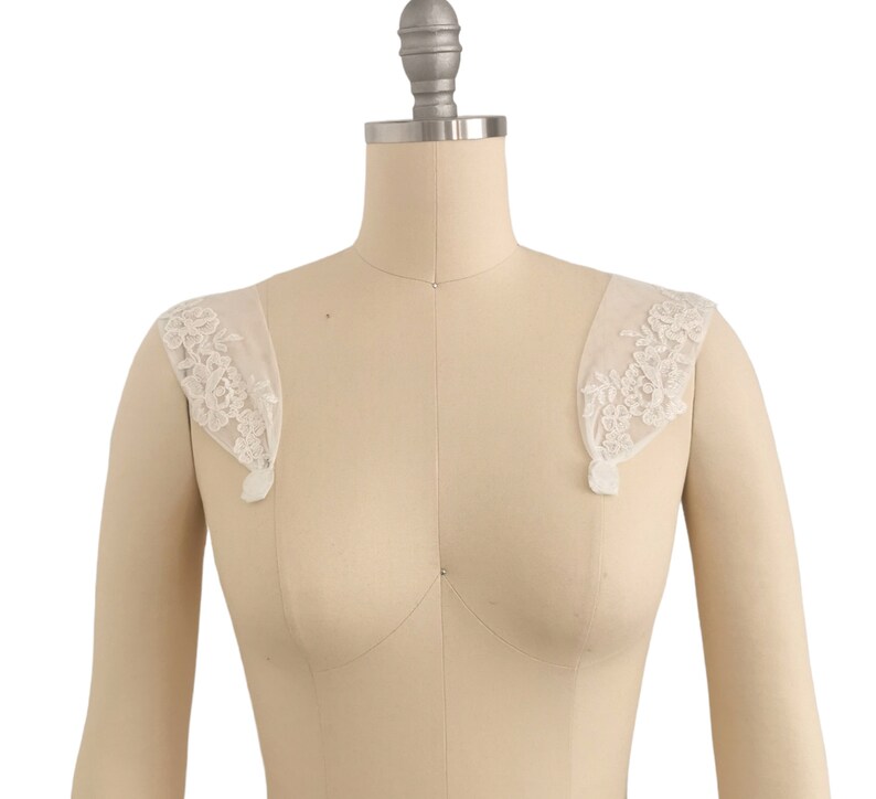 Puede incluir: Un par de tirantes de hombro de encaje blanco para un vestido de novia u otra vestimenta formal.