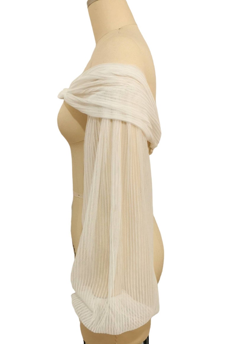 Puede incluir: Top blanco de hombros descubiertos con mangas largas, transparentes y a rayas.