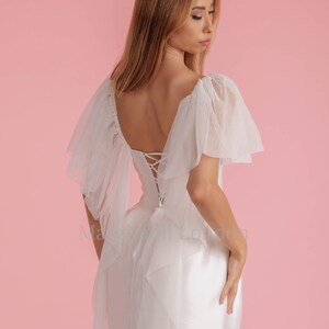 Puede incluir: Un vestido blanco con ribete de encaje y espalda con cordones. El vestido tiene una superposici&oacute;n de tul con mangas con volantes.