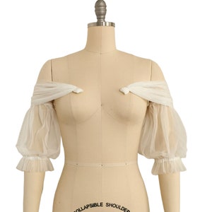 May include: White off-the-shoulder tulle bridal bolero with puffed sleeves and a gathered ruffle trim.