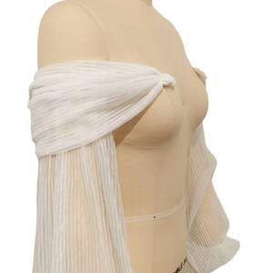 Puede incluir: Bolero de novia blanco, sin hombros, con mangas largas. Las mangas est&aacute;n hechas de una tela transparente y plisada.