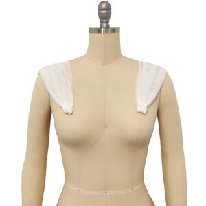 May include: White fabric shoulder pads on a dress form. The shoulder pads are made of a sheer, lightweight fabric and are designed to add volume and shape to the shoulders.