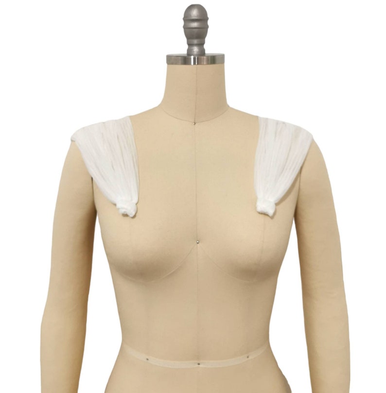 May include: White fabric shoulder pads on a dress form. The shoulder pads are made of a sheer, lightweight fabric and are designed to add volume and shape to the shoulders.