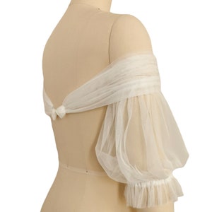 May include: White off-the-shoulder tulle bridal bolero with puffed sleeves and a ruffled trim.