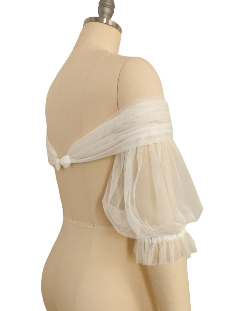 May include: White off-the-shoulder tulle bridal bolero with puffed sleeves and a ruffled trim.