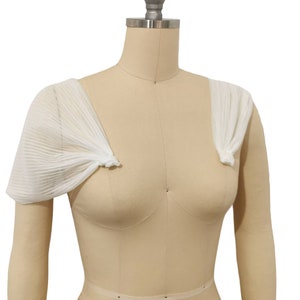 May include: White sheer fabric shoulder wraps with a pleated design. The wraps are tied at the shoulders with a knot.